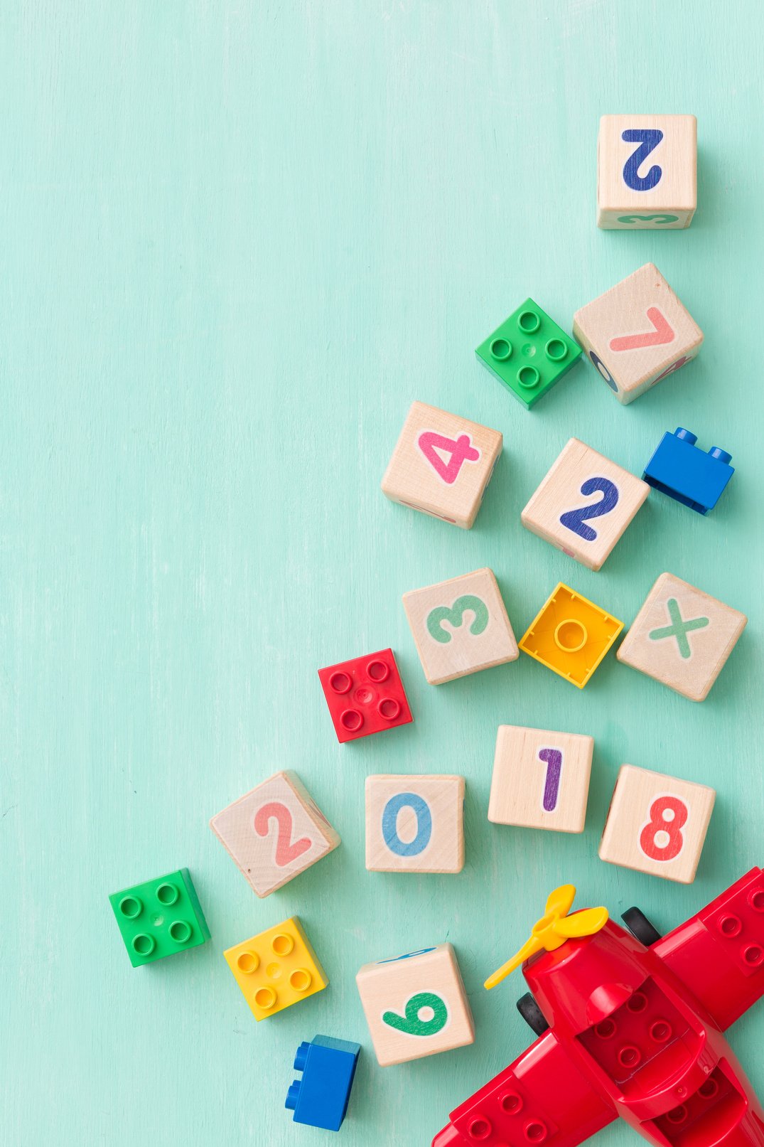 Wooden cubes with numbers and colorful toy bricks on a turquoise wooden background.